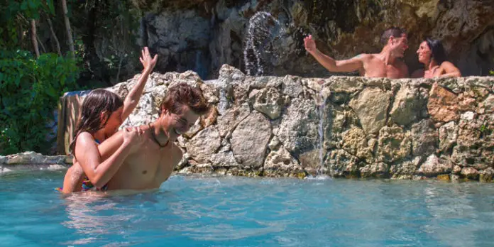 4 people swimming in a waterfall